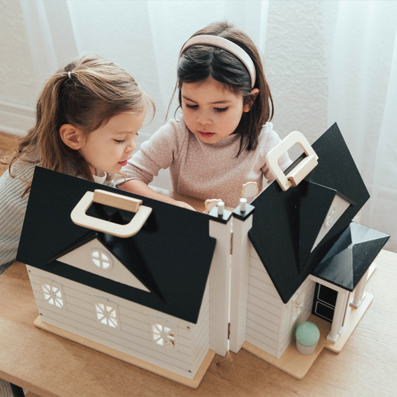 Two children playing with a toy house on a wooden floor.