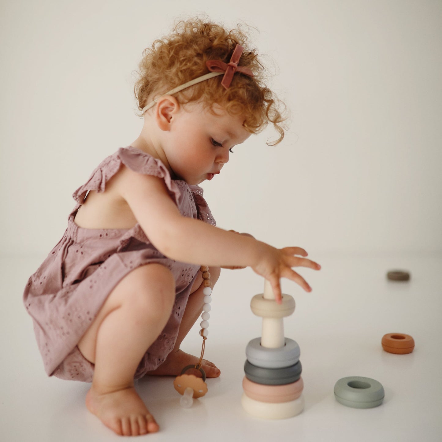 Child playing with a stack of colorful wooden rings on a plain background