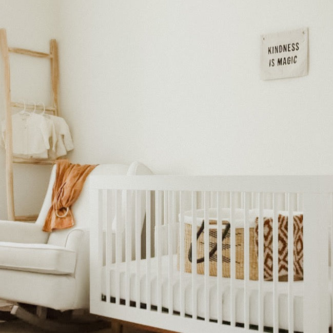 Nursery room with a white crib, beige sofa, and wooden clothes rack.