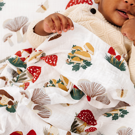 Baby wrapped in a blanket with a forest-themed pattern, surrounded by Christmas decorations.