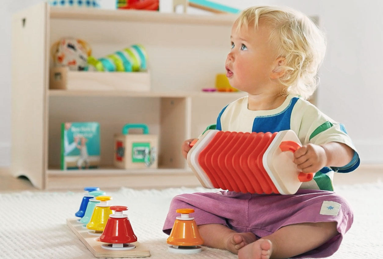 Child playing with a red toy instrument in a room with shelves and toys.