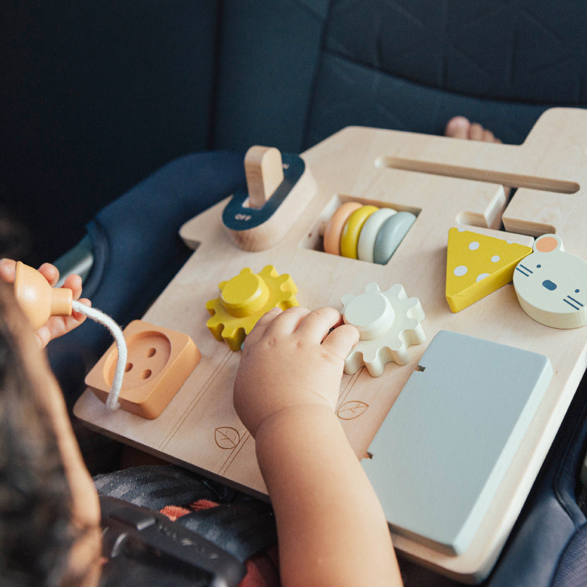 Child playing with a wooden toy set in a car seat