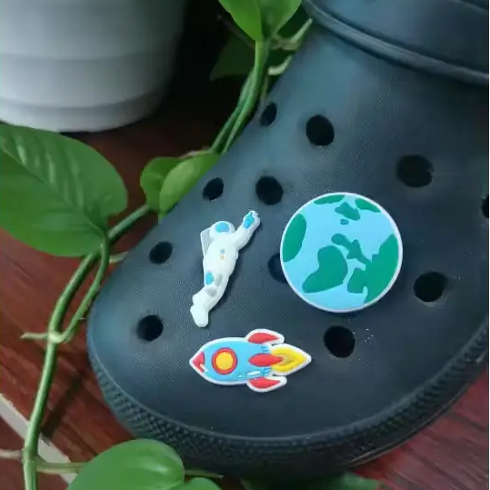 Black clog shoe with space-themed stickers on a wooden surface with green leaves.