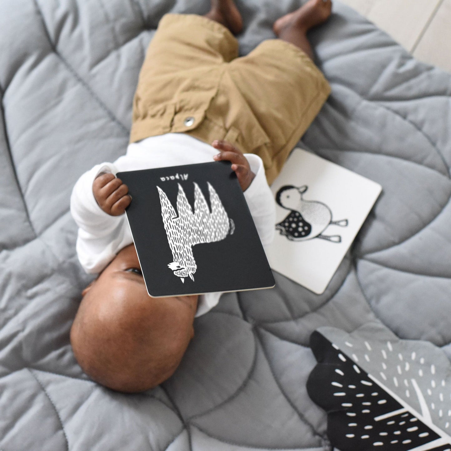 Child holding a black card with white design on a gray quilted surface