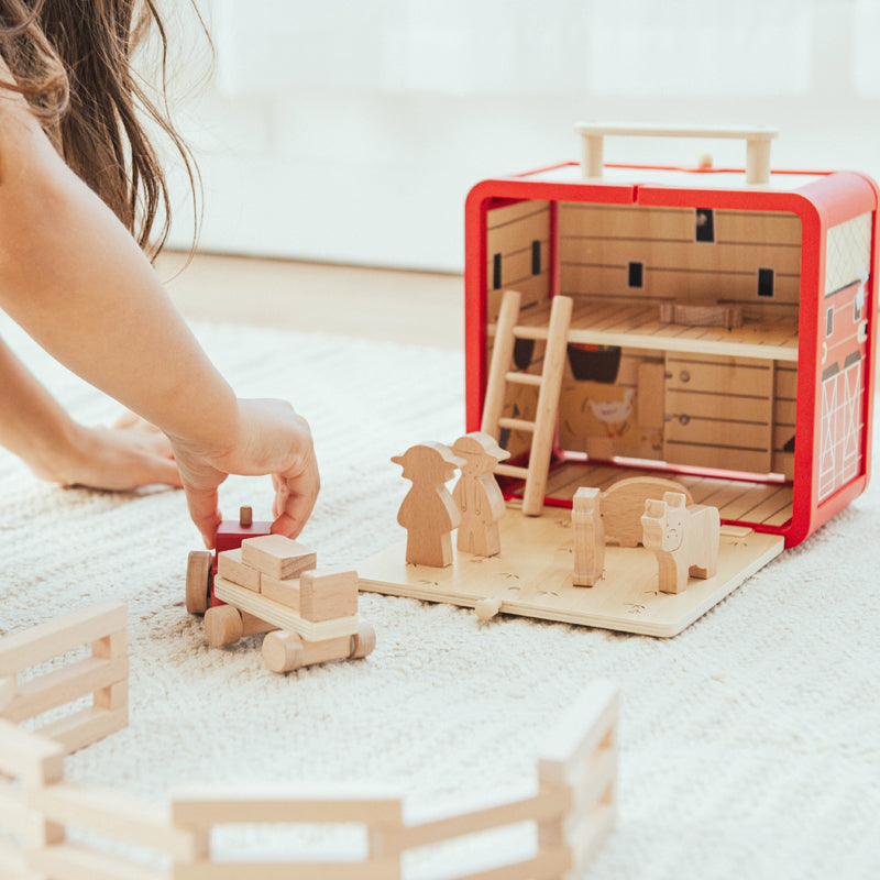Child playing with wooden farm toys on a light-colored floor.