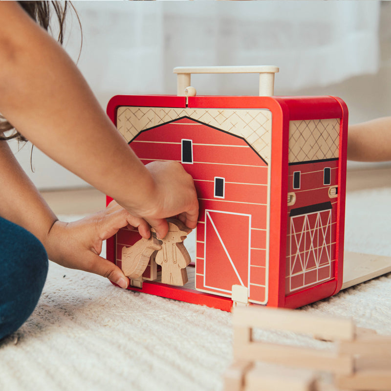 Child playing with a wooden barn toy set on a light-colored floor.
