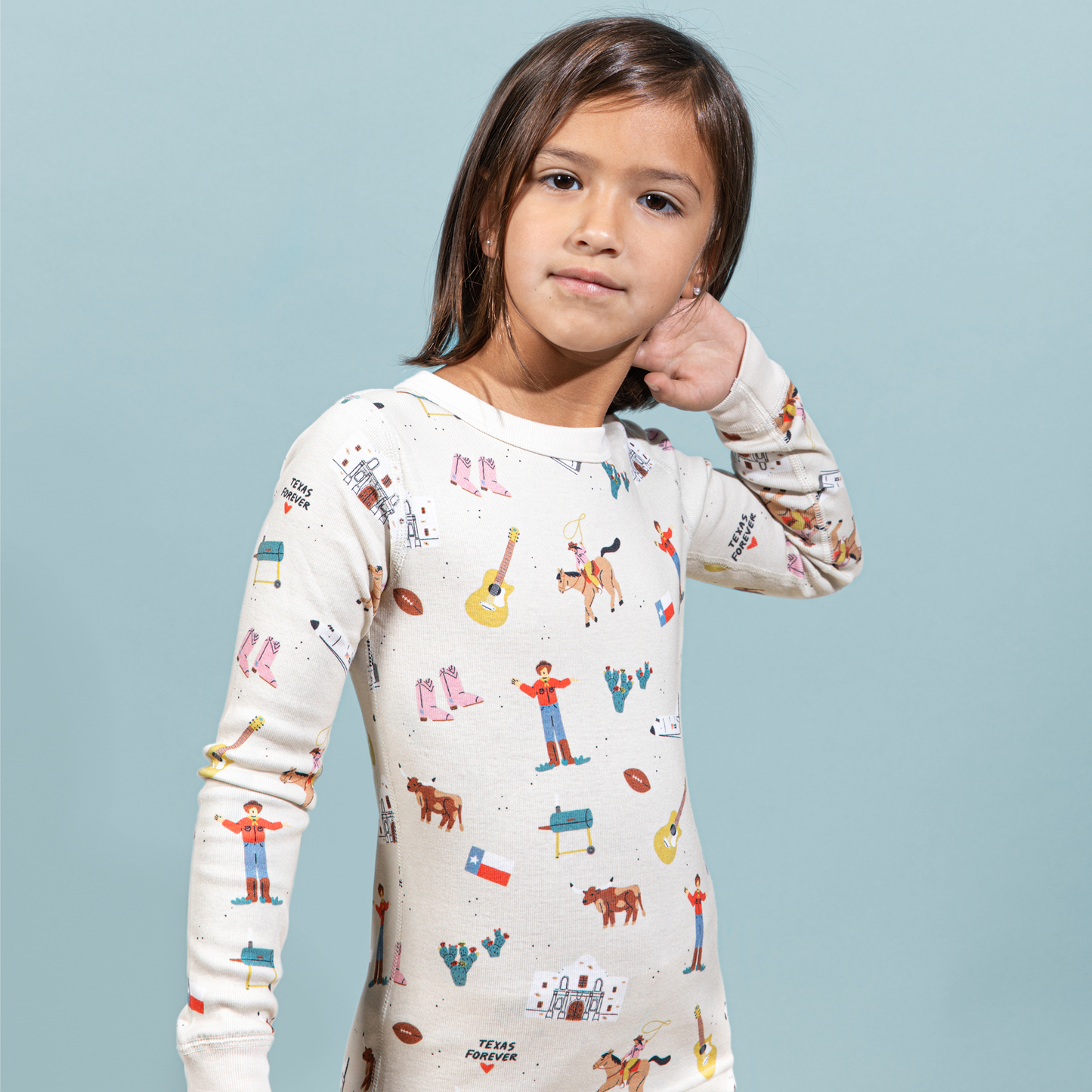Child wearing a Texas themed pajama shirt with colorful patterns on a light blue background