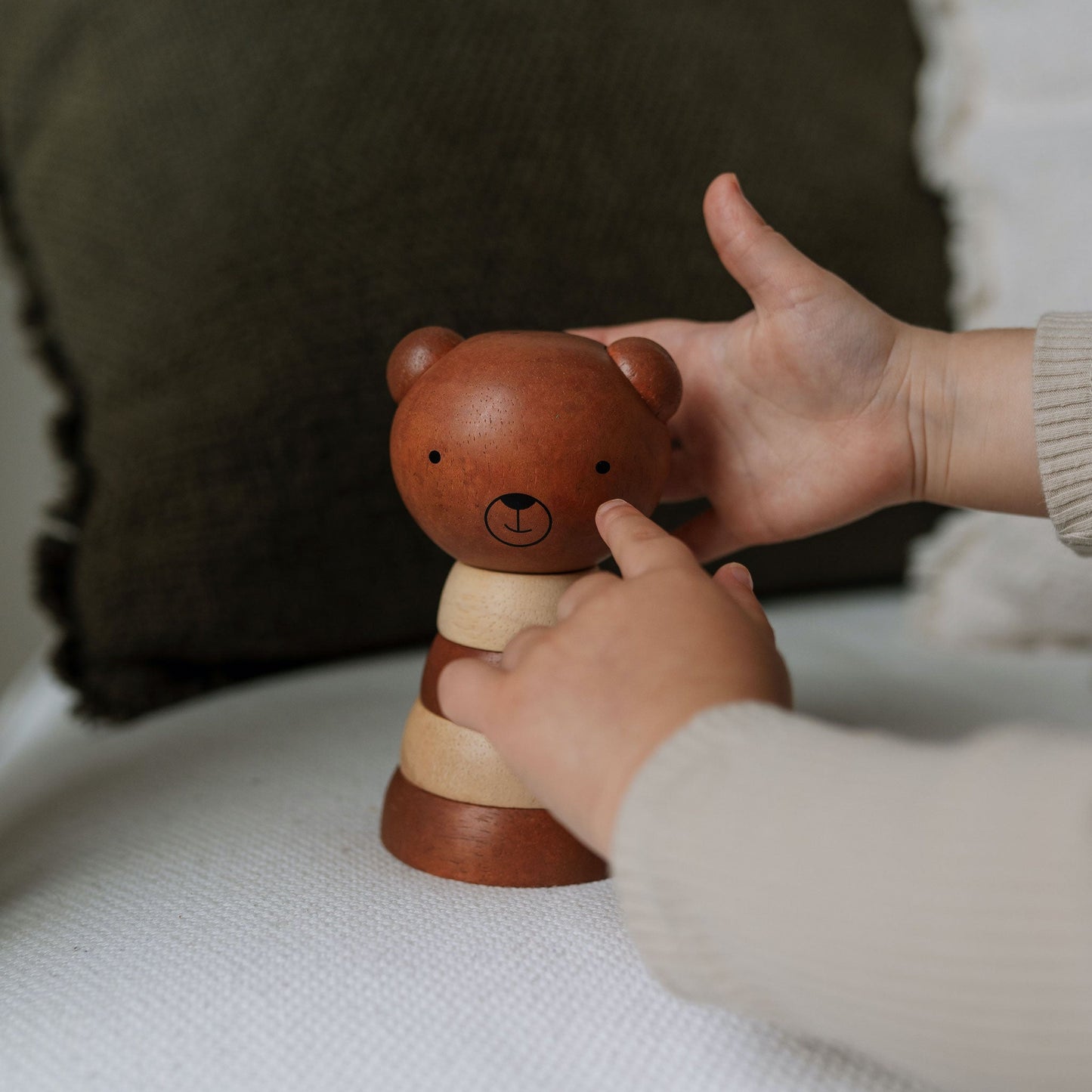 Wooden bear stacker toy being held by a child's hands on a soft surface.
