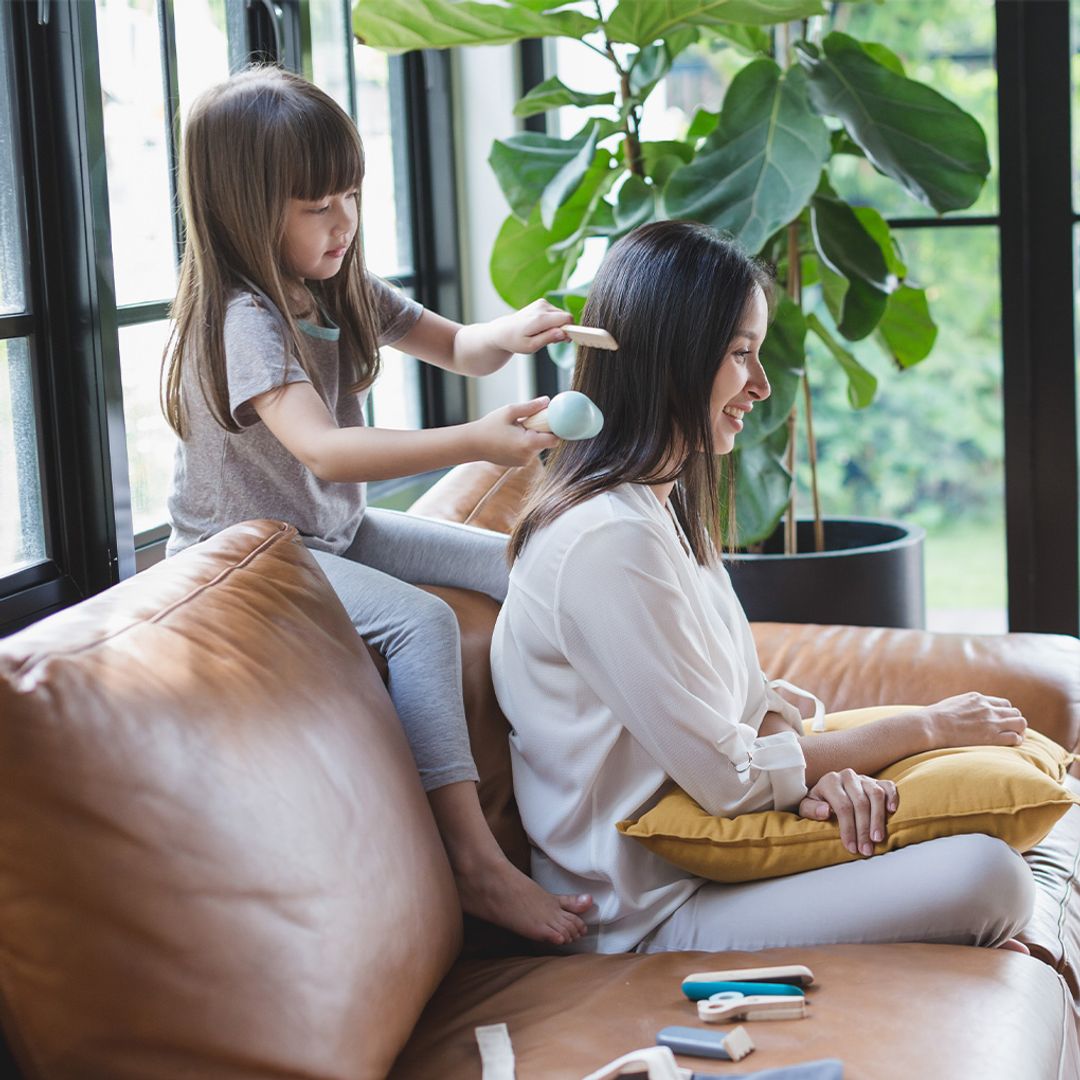Child and mother playing with pretend hairdresser kit on a brown leather couch.