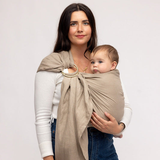 Woman holding a baby in a beige wrap against a white background