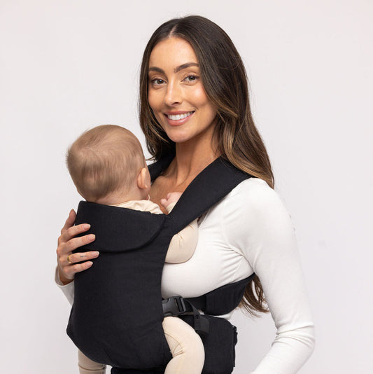 Woman holding a baby in a black baby carrier against a white background