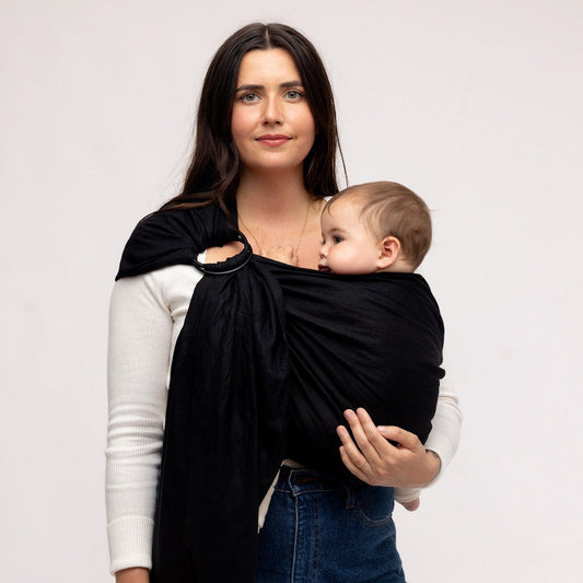 Woman holding a baby in a black wrap against a plain background