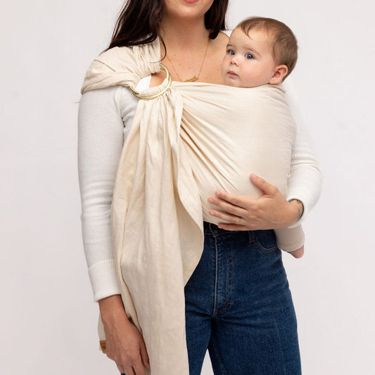 Woman holding a baby in a beige baby wrap against a white background