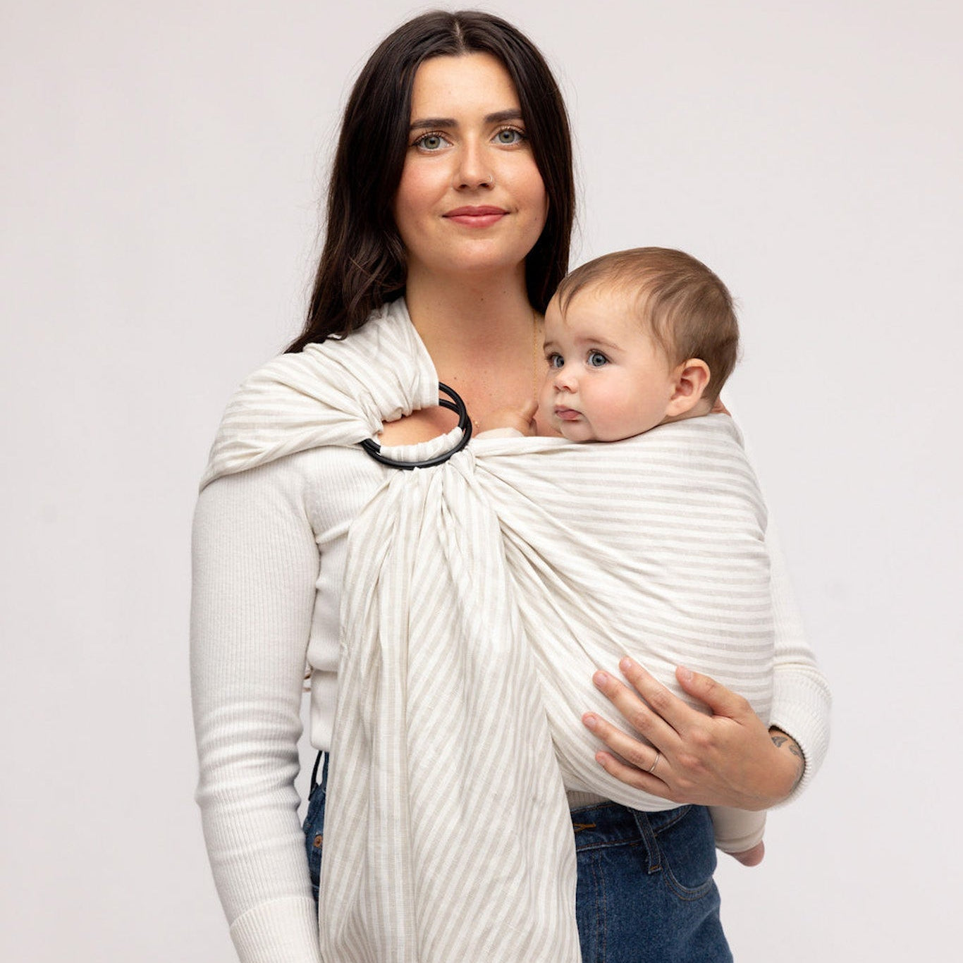 Woman holding a baby in a white woven carrier against a plain background