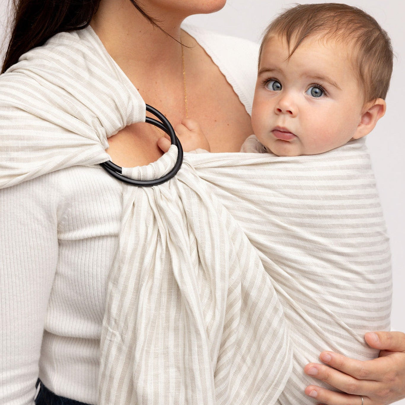 Woman holding a baby in a white sling against a plain background