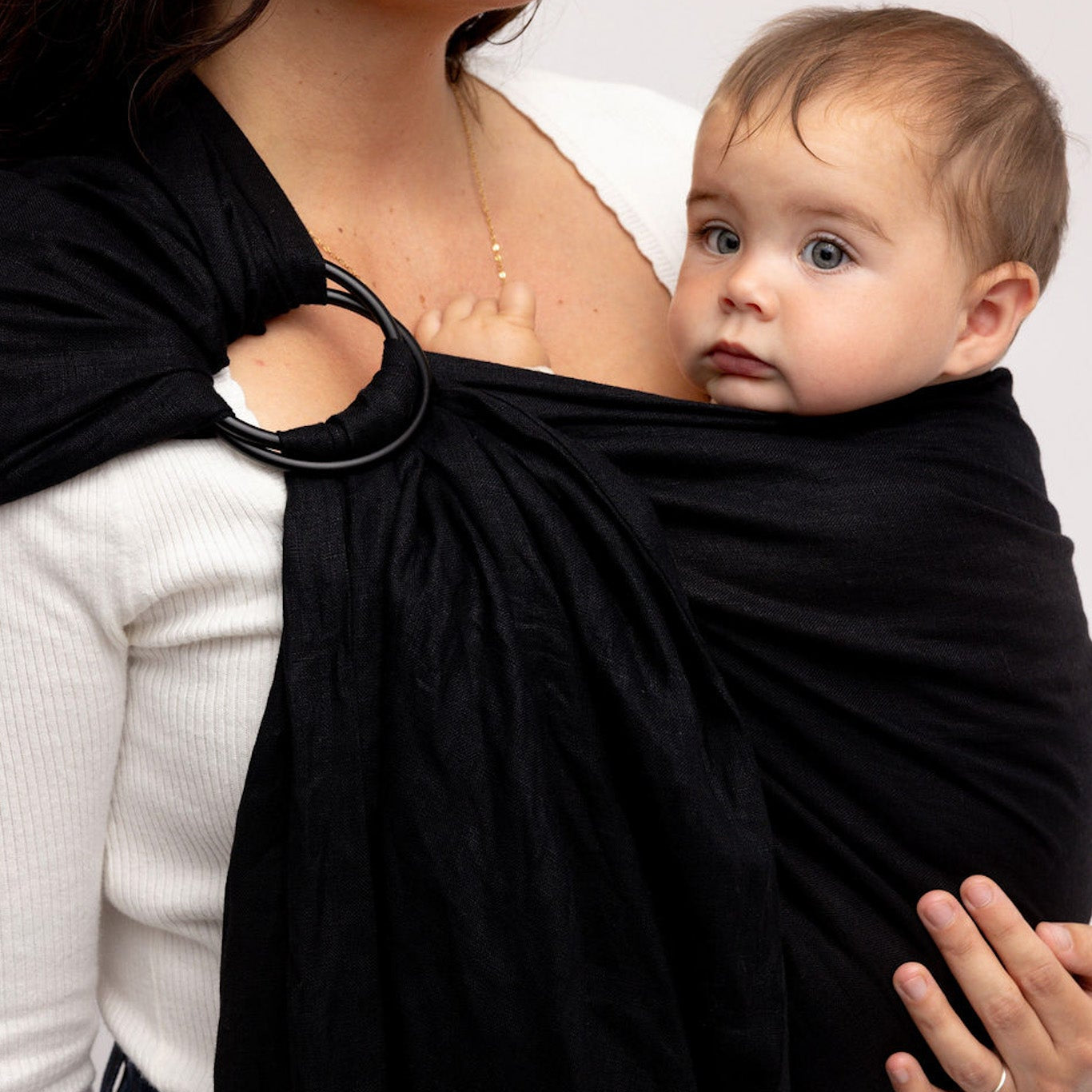 Woman holding a baby in a black sling against a white background