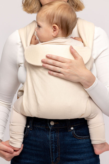 Person holding a baby in a beige baby carrier against a plain background