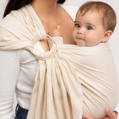 Woman holding a baby in a beige ring sling against a white background
