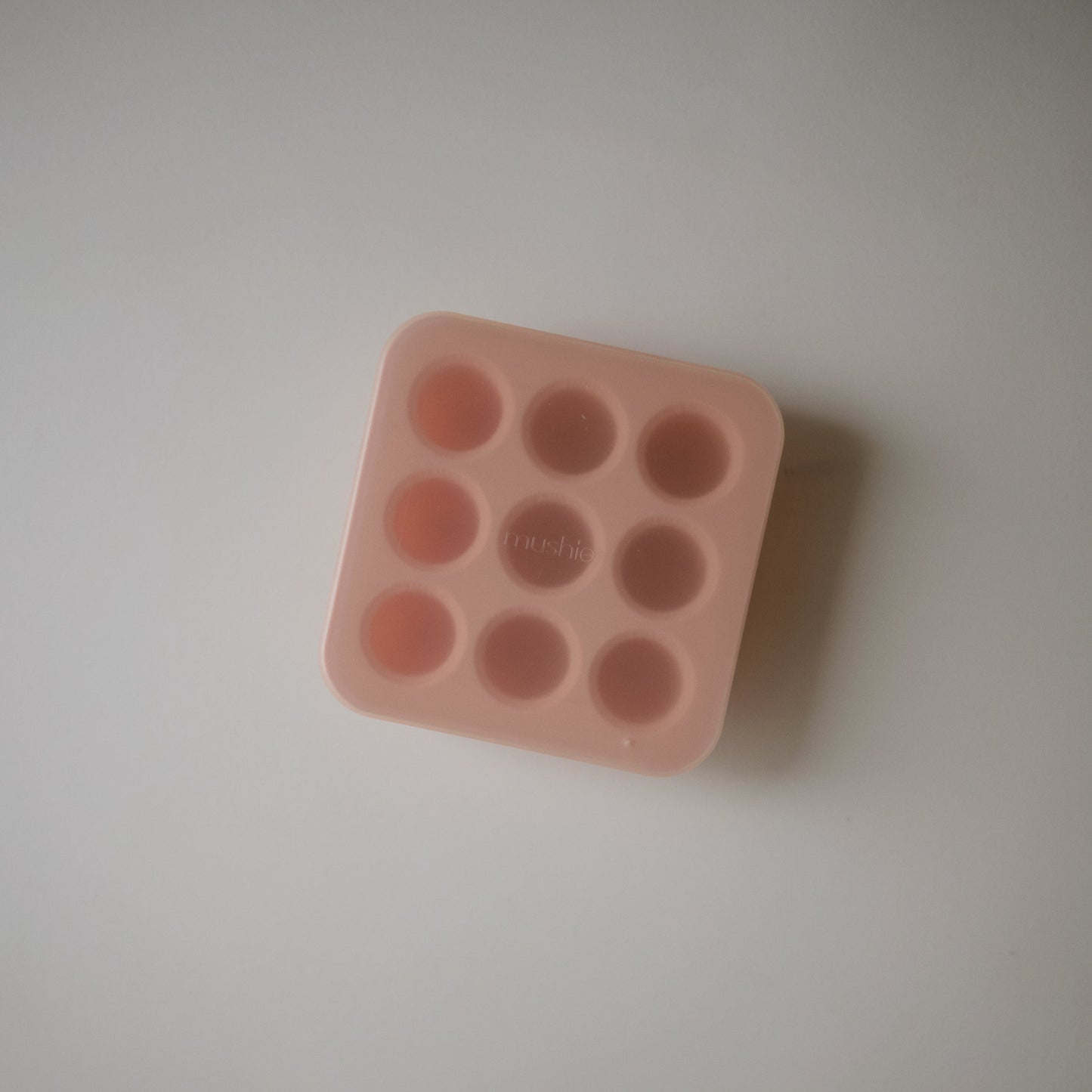 Pink silicone mold with multiple small round cavities on a light gray background