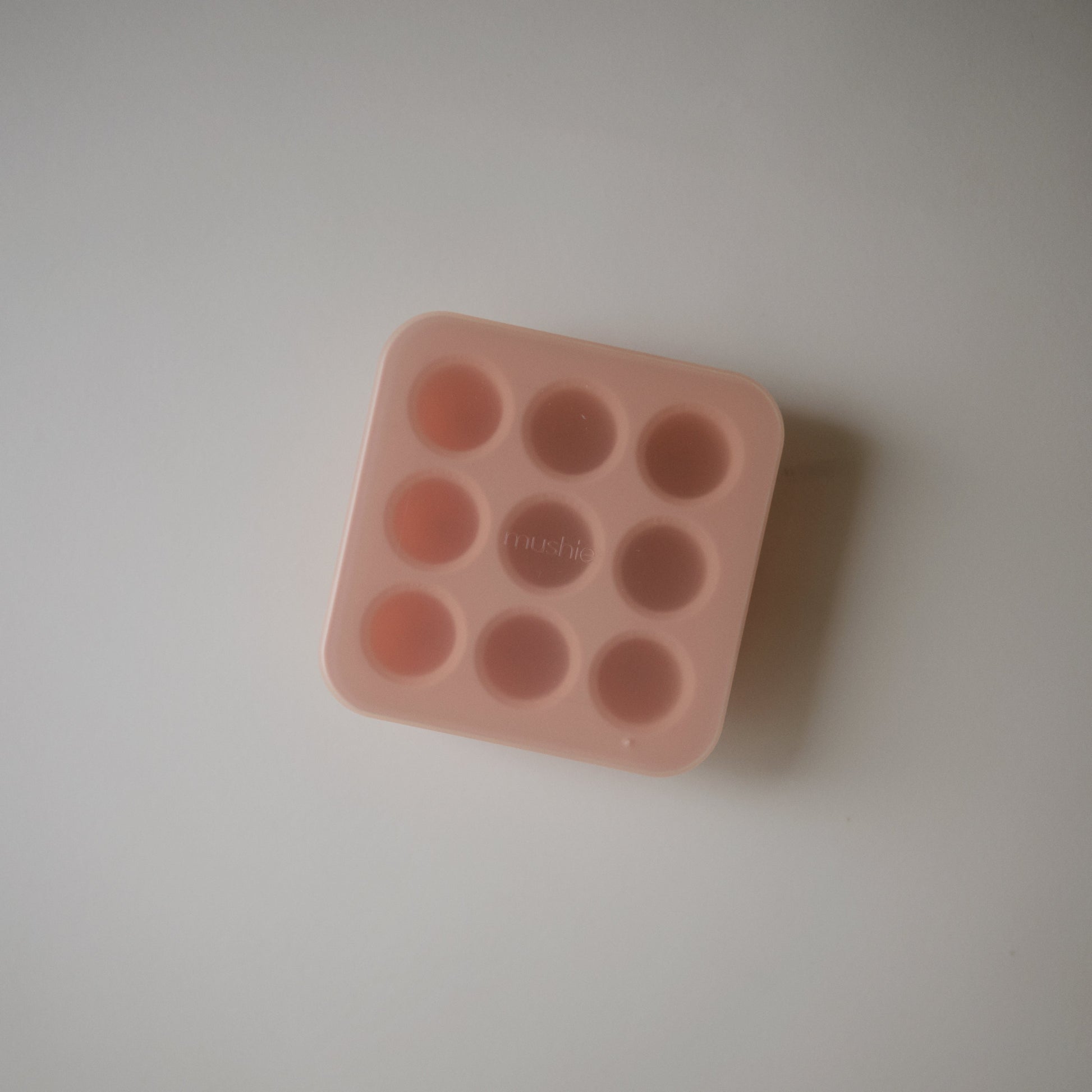 Pink silicone mold with multiple small round cavities on a light gray background