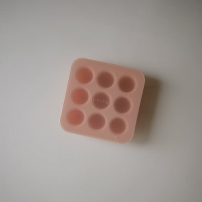 Pink silicone mold with multiple small round cavities on a light gray background