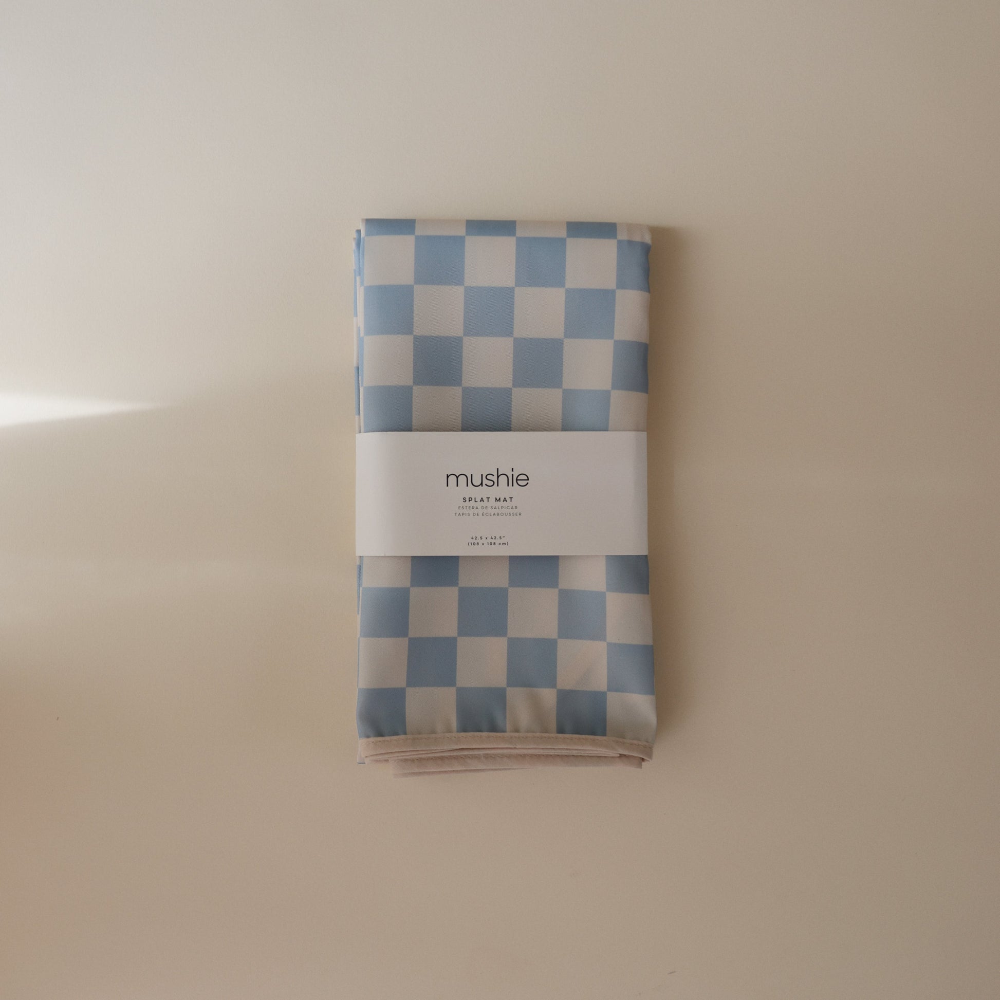 Folded blue and white checkered blanket with 'mushie' branding on a beige background