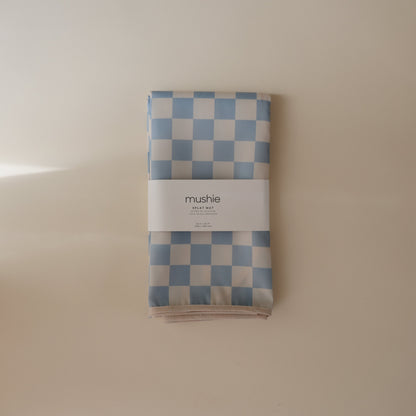 Folded blue and white checkered blanket with 'mushie' branding on a beige background