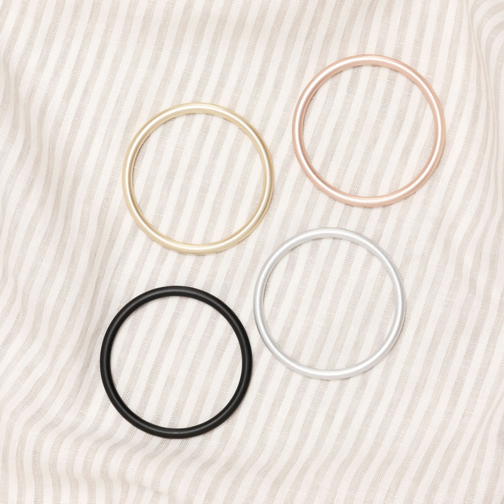 Four hair ties in gold, pink, black, and white on a textured beige background