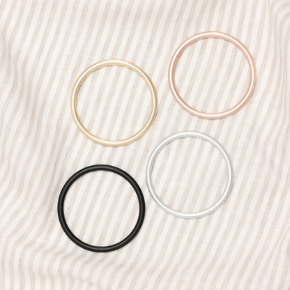 Four hair ties in gold, pink, black, and white on a textured beige background