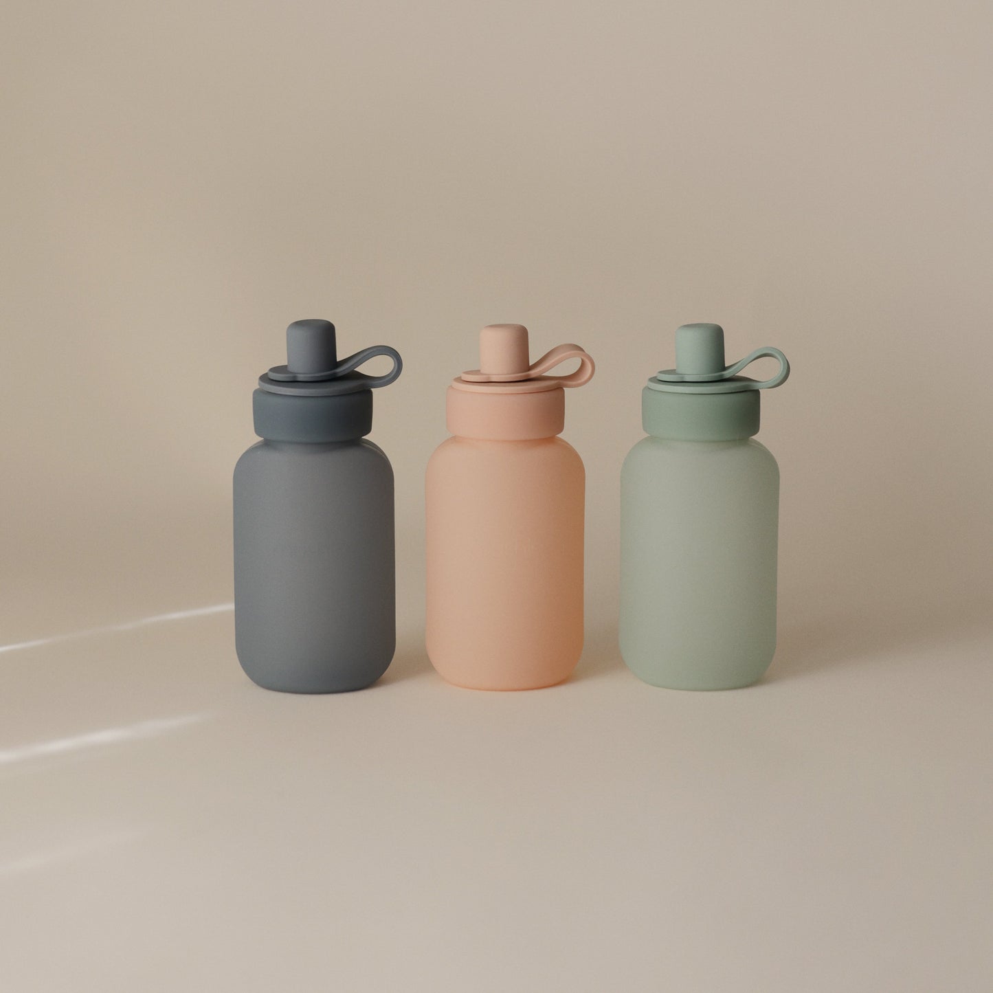 Three colorful water bottles with different shades on a beige background