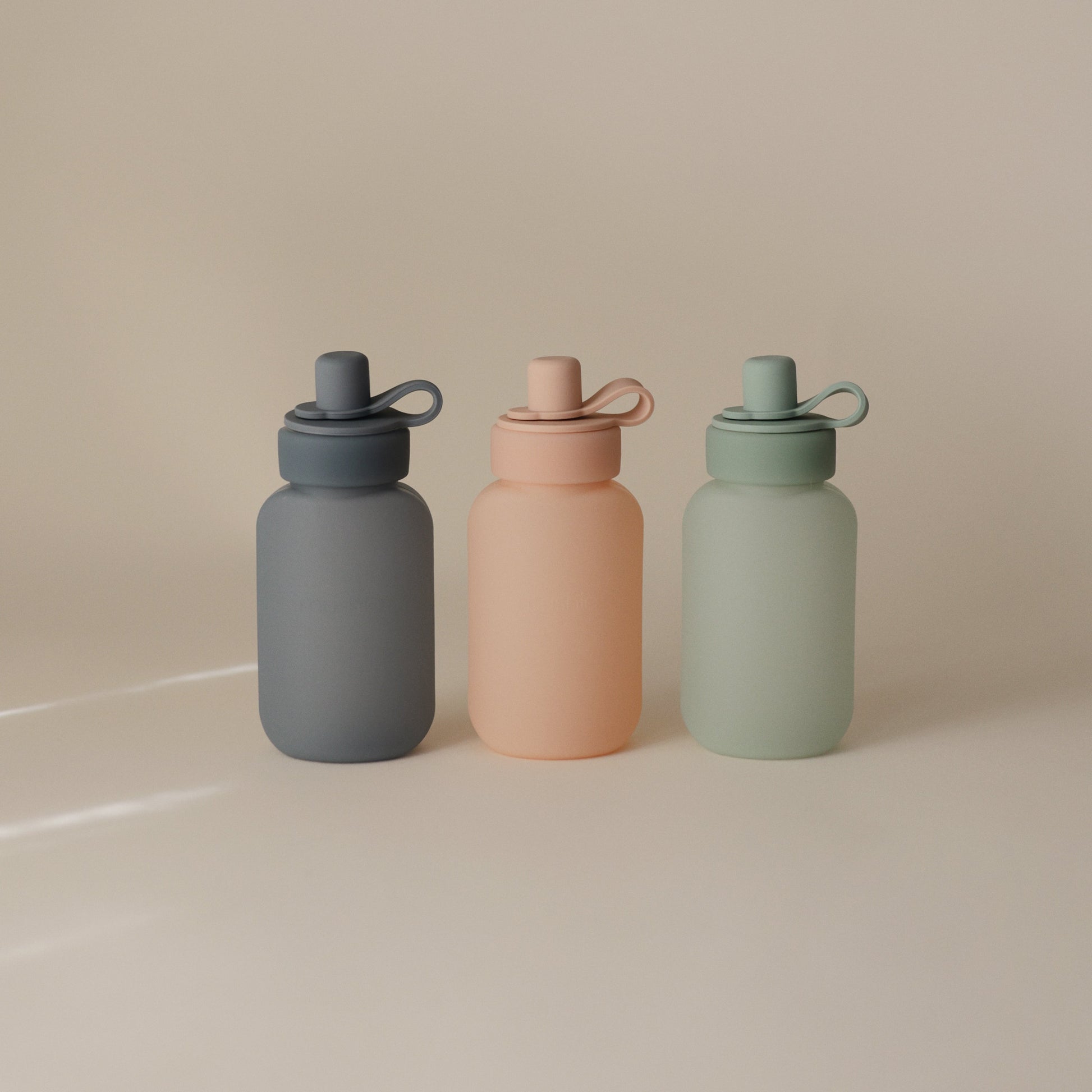 Three colorful water bottles with different shades on a beige background