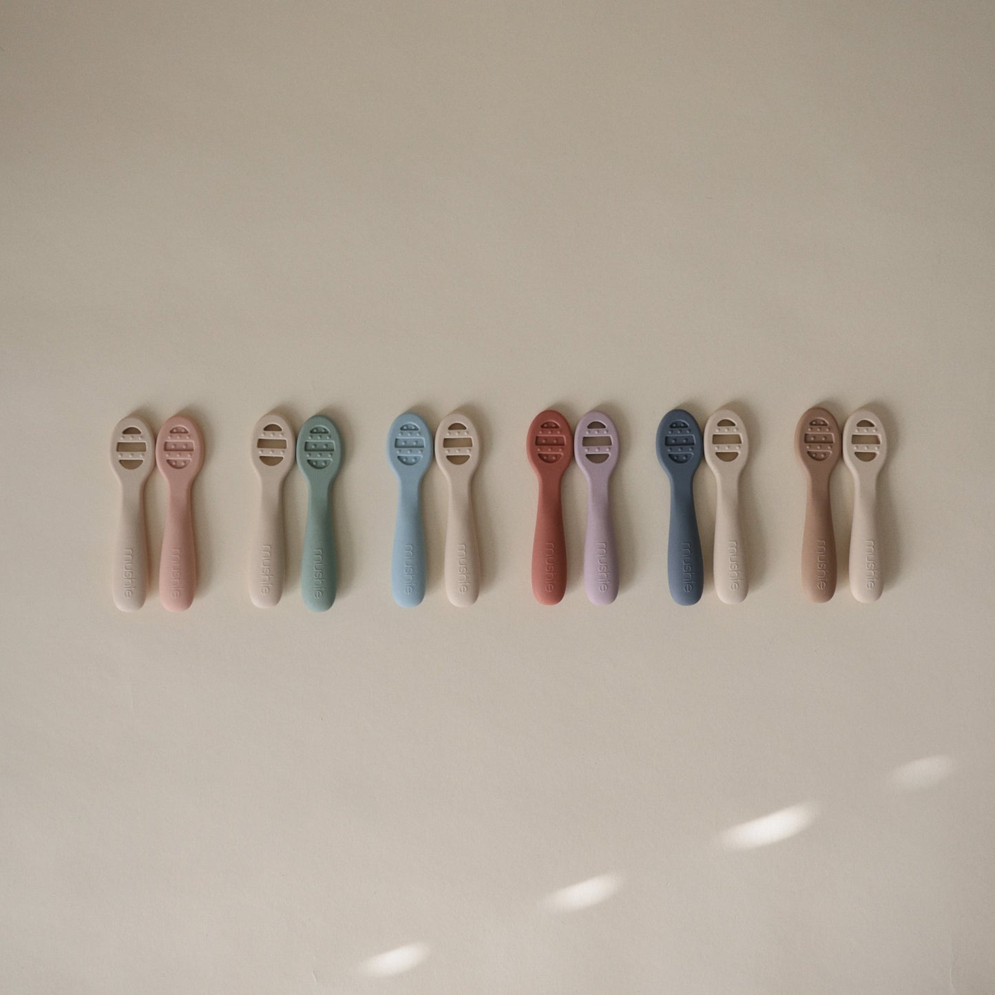 Row of baby teethers in various pastel colors on a light background