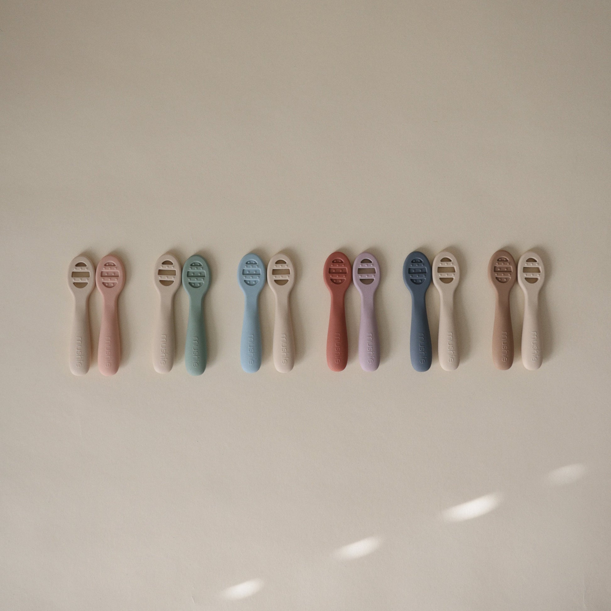 Row of baby teethers in various pastel colors on a light background