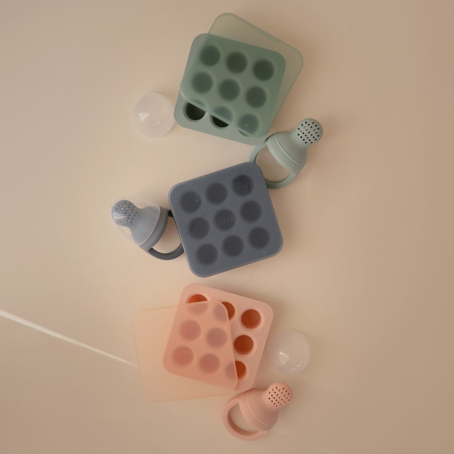 Set of silicone baby bottle molds in green, gray, and pink on a beige background