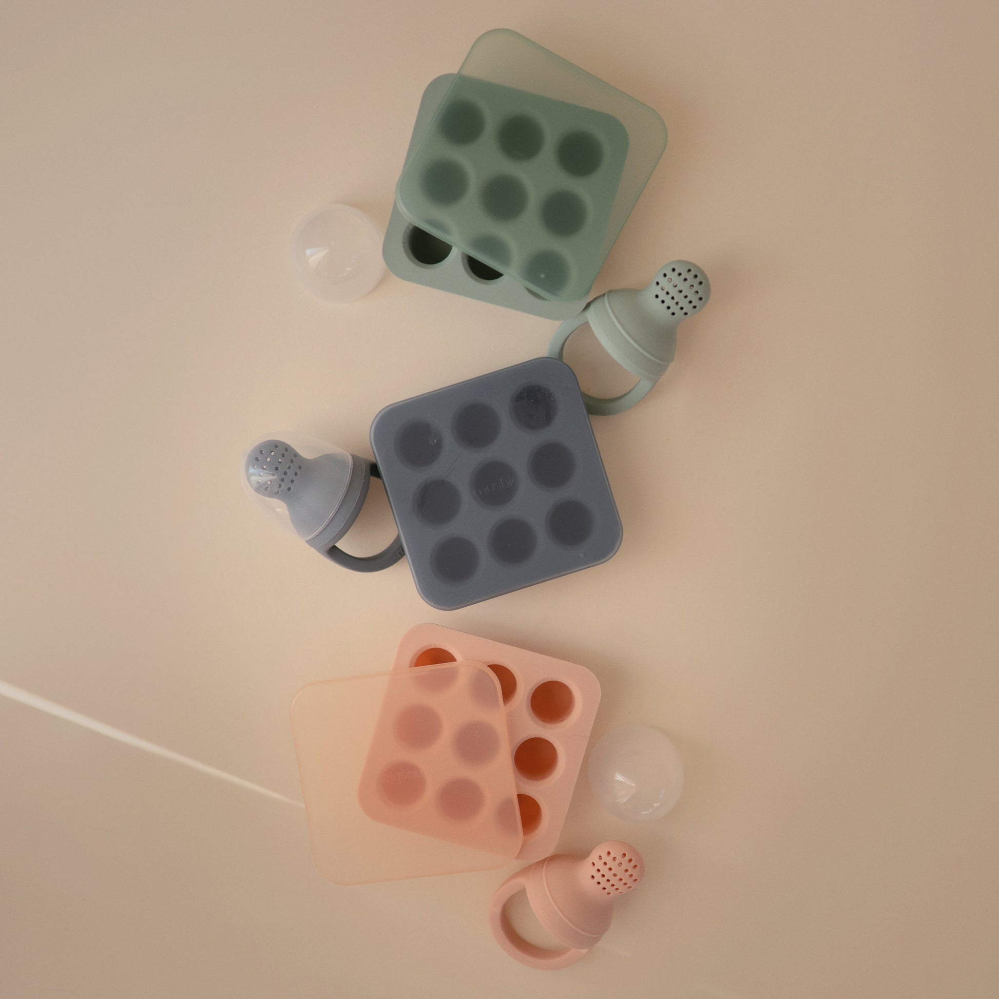 Set of silicone baby bottle molds in green, gray, and pink on a beige background