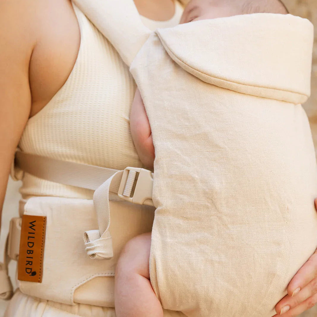 Baby being carried in a beige baby carrier with a blurred background