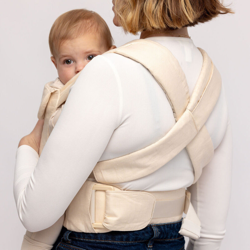 Woman wearing a baby in a beige carrier against a white background