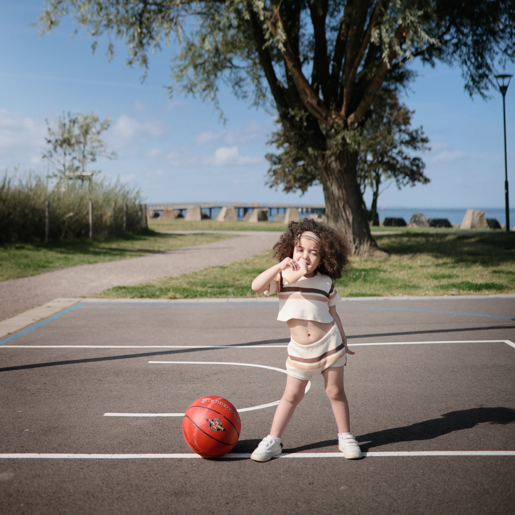 Child playing basketball on an outdoor court with a scenic background