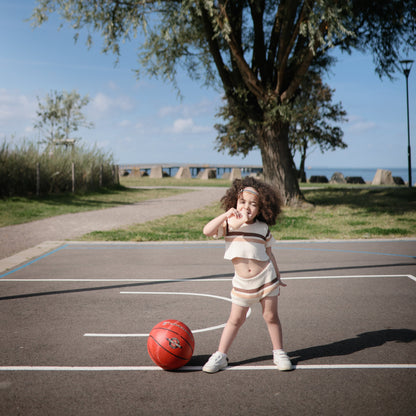 Child playing basketball on an outdoor court with a scenic background