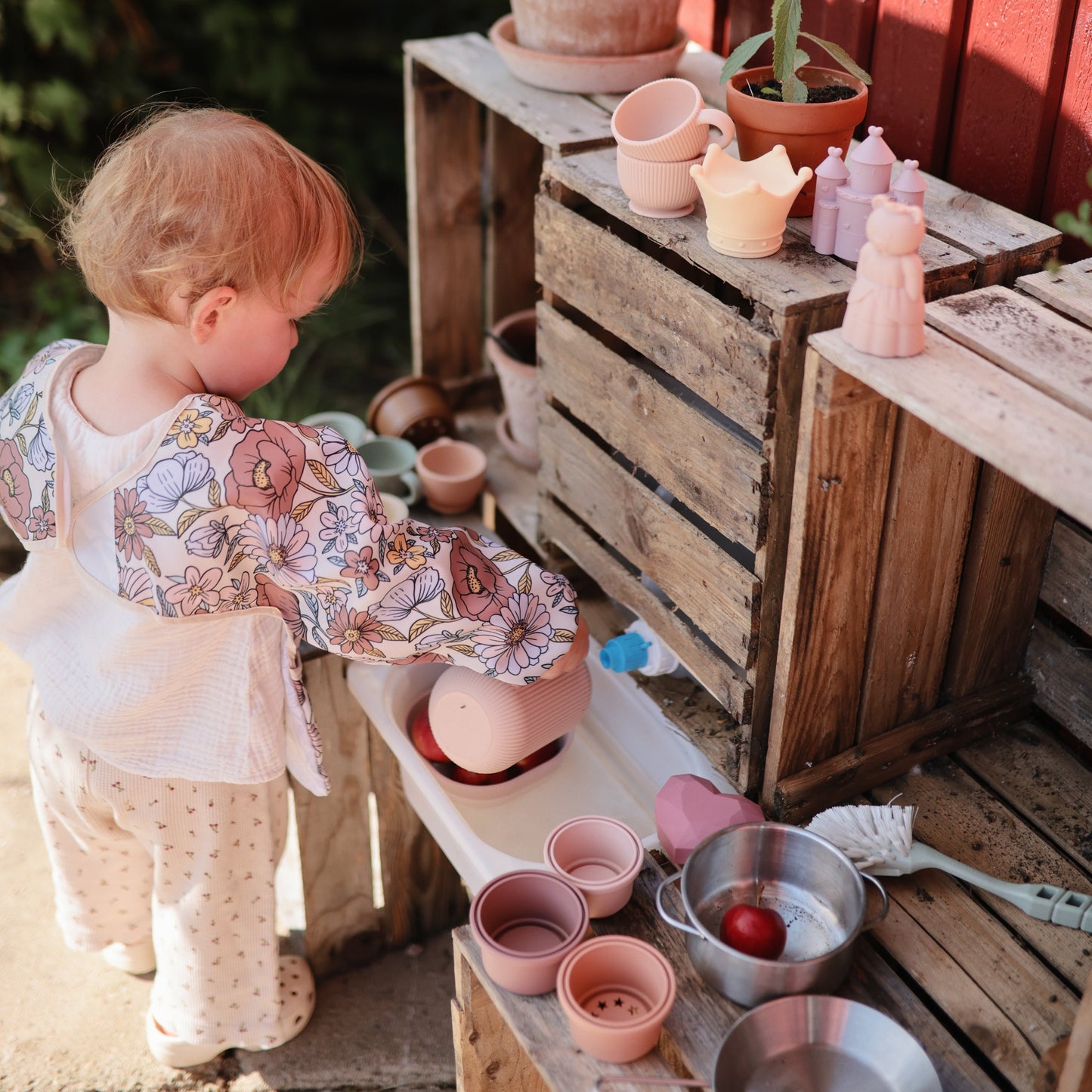 Child playing with pots and pans on a wooden surface outdoors