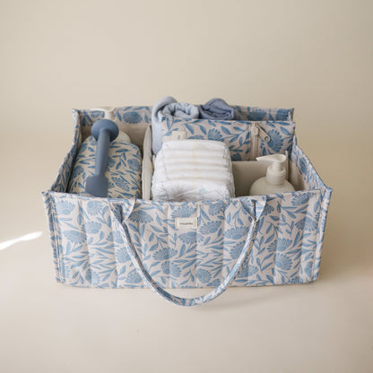 Fabric caddy with baby items including diapers and a bottle on a beige background