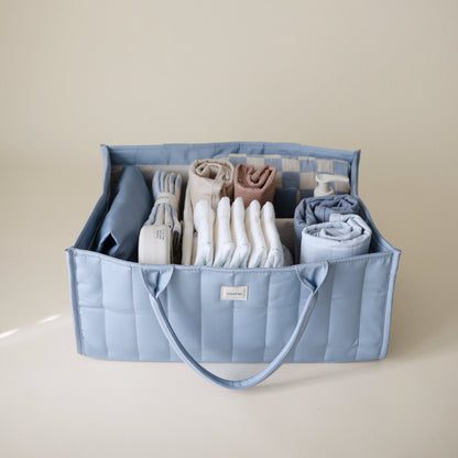 Blue storage caddy with folded clothes on a beige background