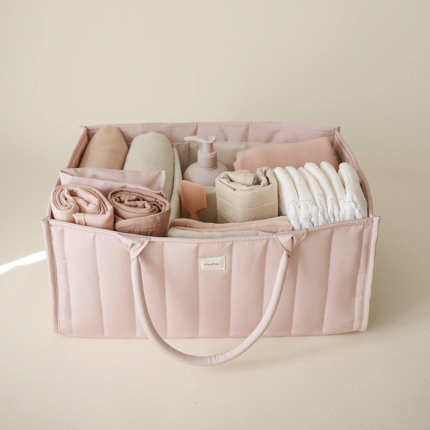 Pink organizer bag with baby items on a beige background