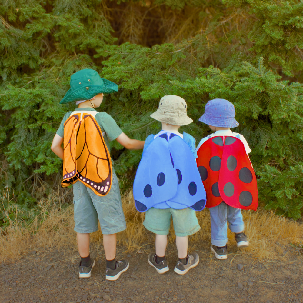 Three children in nature wearing butterfly and ladybug costumes.
