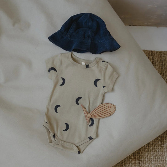 Baby romper with fish design and blue hat on a white surface