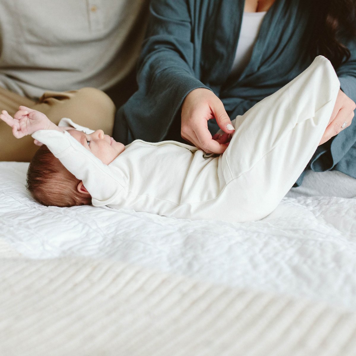 Baby lying on a bed with a person adjusting the baby's clothing