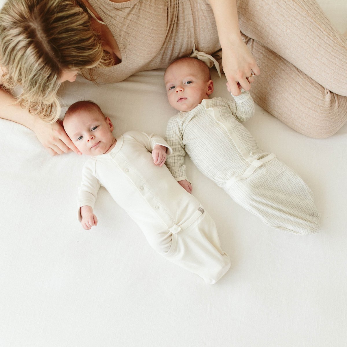 Woman with two swaddled babies on a white blanket