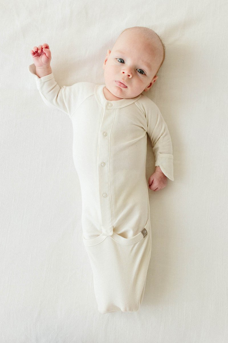 Baby wearing a cream-colored onesie lying on a white surface