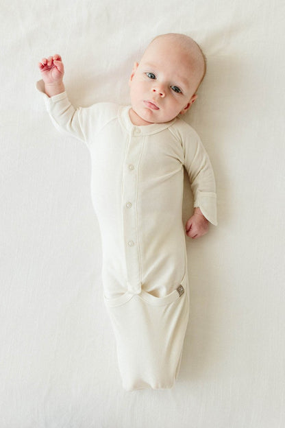 Baby wearing a cream-colored onesie lying on a white surface