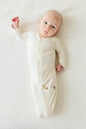 Baby wearing a cream-colored onesie lying on a white surface